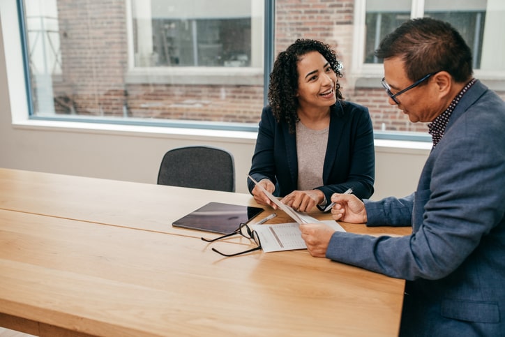 Two people sit at a wooden table in an office