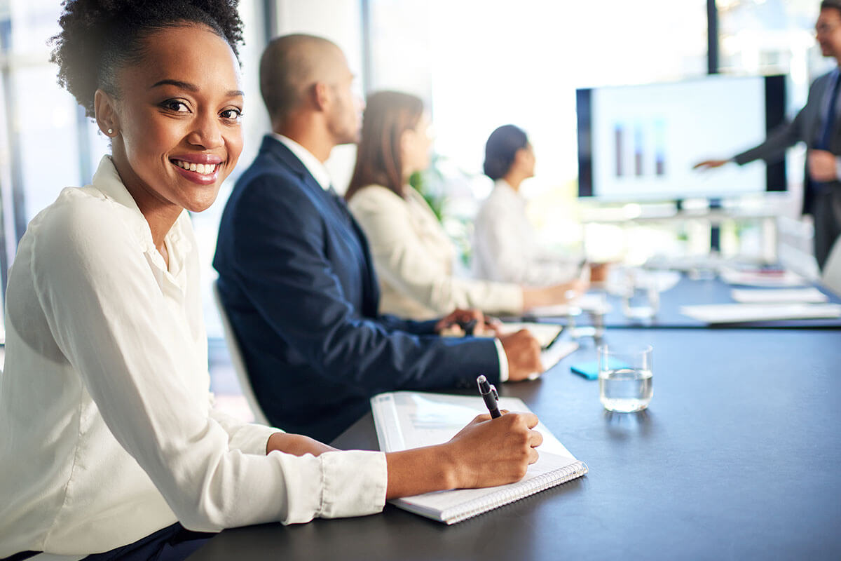 A smiling woman taking notes in a business meeting with colleagues