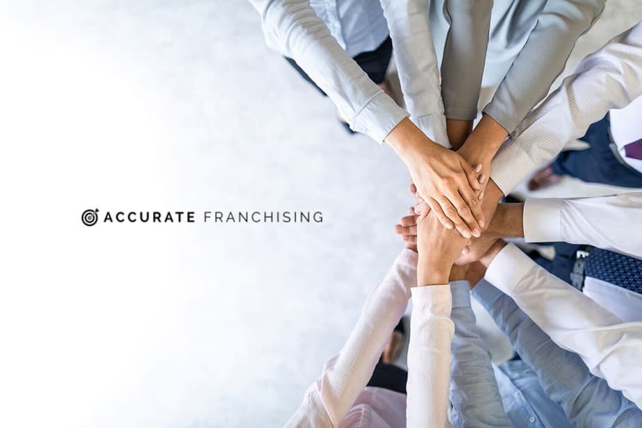 A group of people stack their hands together in a gesture of teamwork next to the Accurate Franchising name