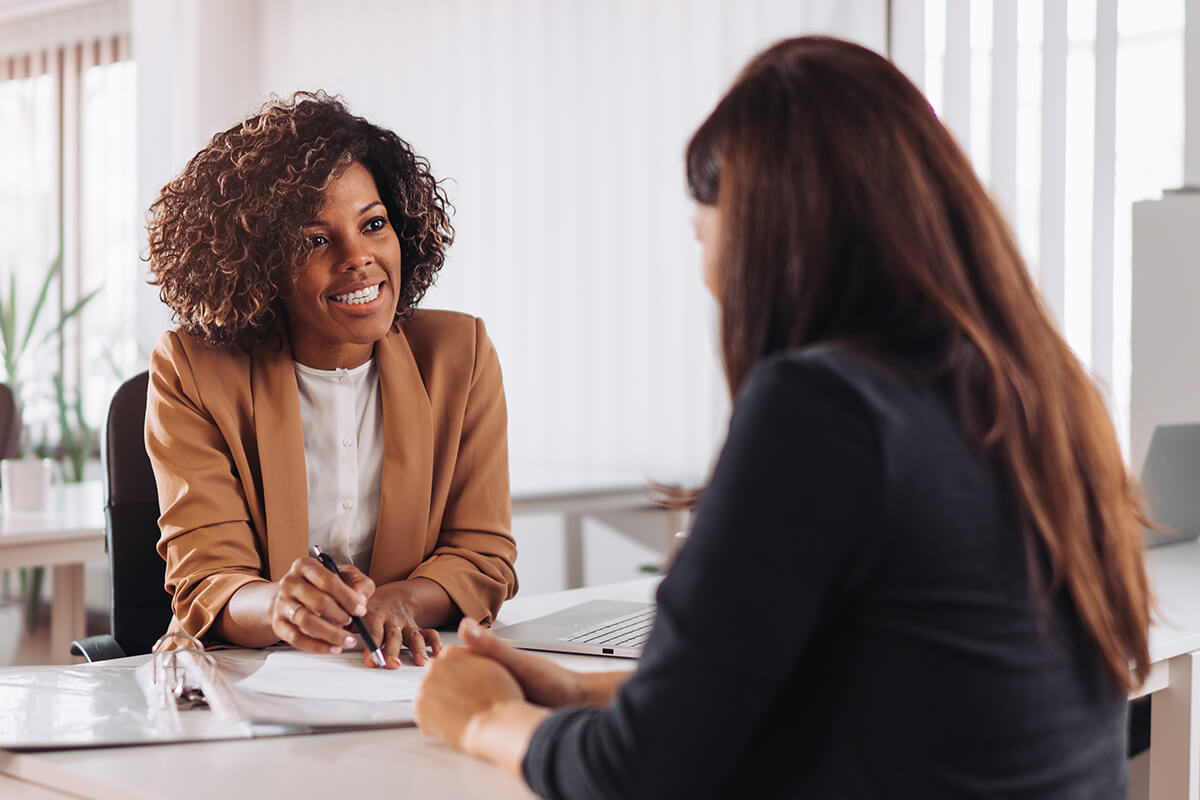 Two women sit across from each other at a desk in an office